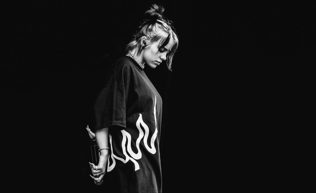 Billie Eilish in a black-and-white photo, standing with her head bowed in a reflective pose, evoking grief and loss.