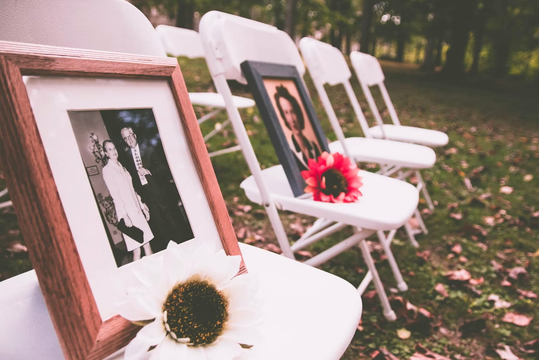 Outdoor celebration of life memorial with framed photographs, flowers and white chairs