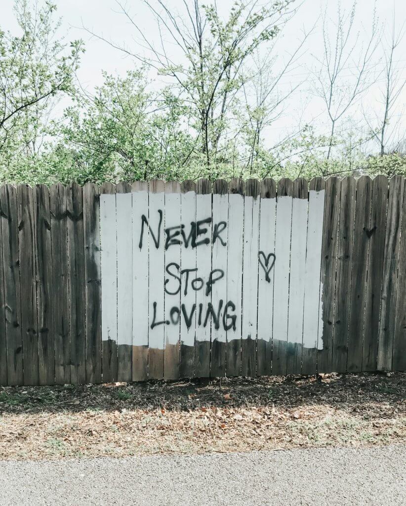Spray-painted fence reading ‘Never Stop Loving,’ a reminder that love continues after loss.