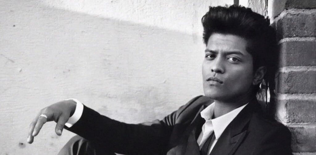 Black-and-white portrait of Bruno Mars leaning against a brick wall, accompanying a music review of “Talking to the Moon.”