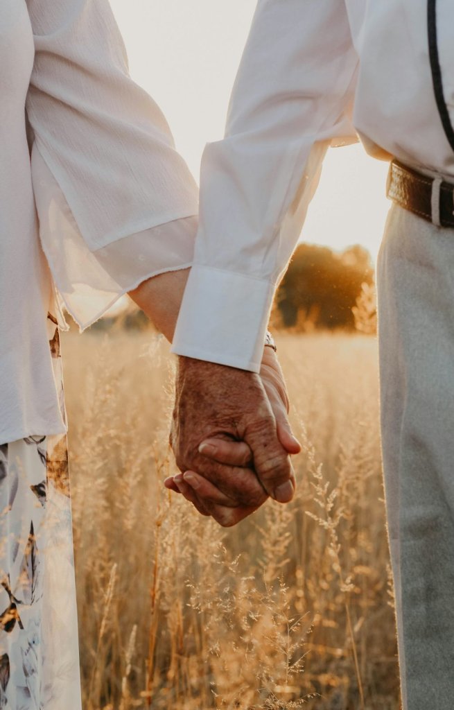 Close-up of an older couple holding hands in a golden field at sunset, symbolizing lasting love and companionship