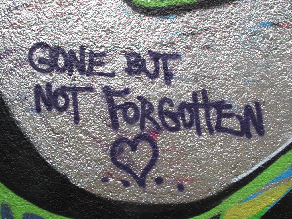 Graffiti reading "Gone but not forgotten," serving as a visual metaphor for digital immortality and AI grief-bots.