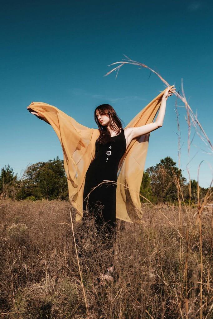 Woman in a black dress holding flowing orange fabric in a field for a Halloween-themed celebration of life