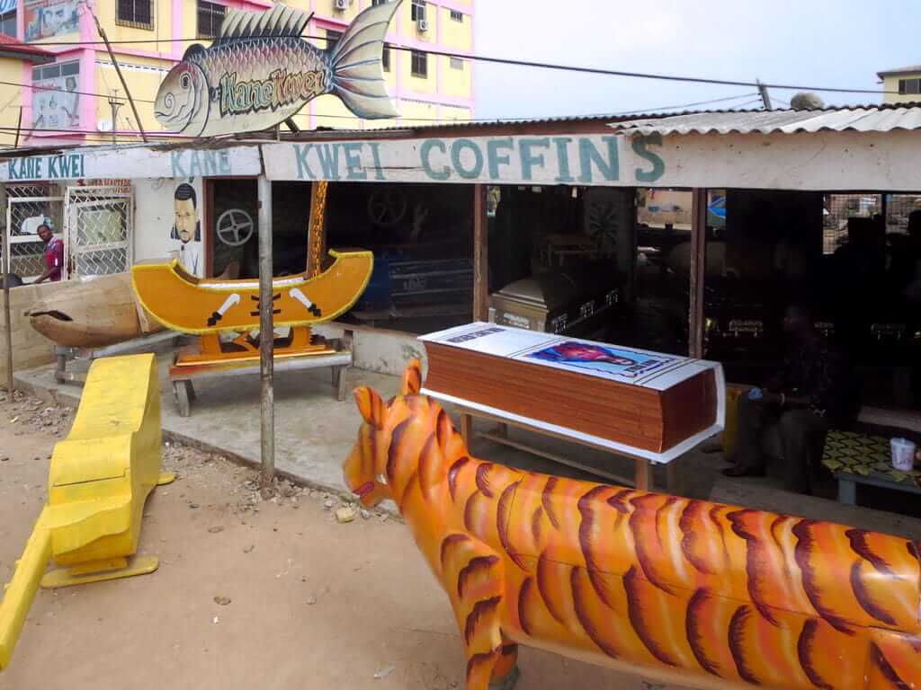 Exterior of the Kane Kwei Carpentry Workshop in Ghana featuring hand-carved fantasy coffins shaped like a tiger and boat.