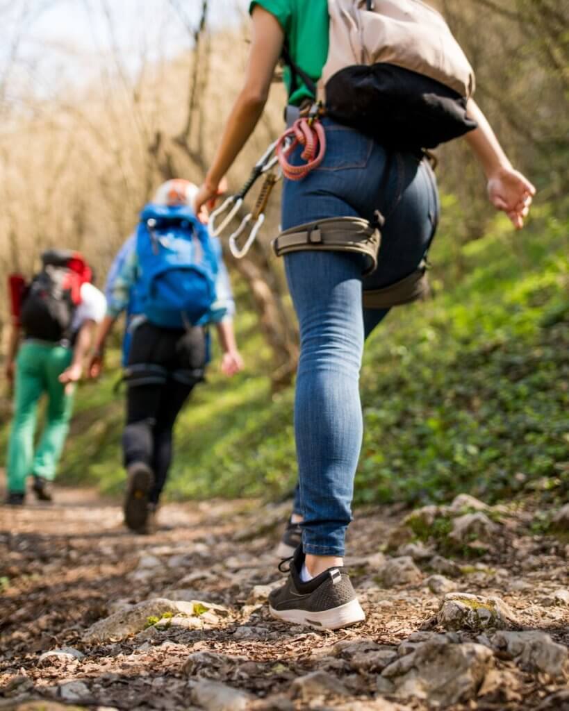 A group of hikers wearing backpacks walks along a rocky, wooded trail, illustrating outdoor activities used in nature-based grief support.