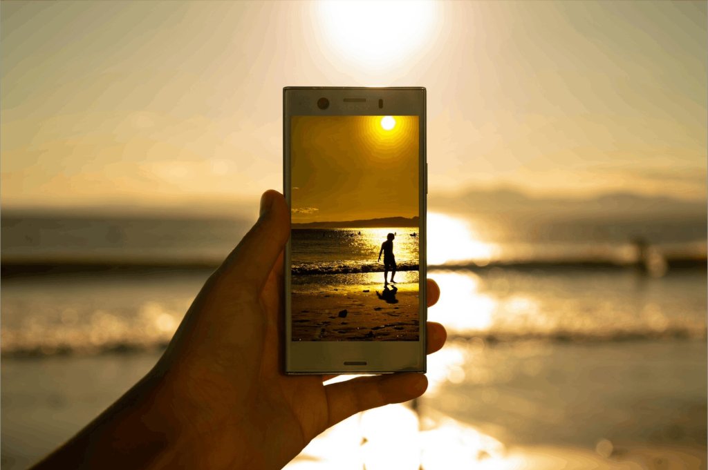 Hand holding a smartphone displaying a photo of a person walking along a beach at sunset, symbolizing memories and remembrance