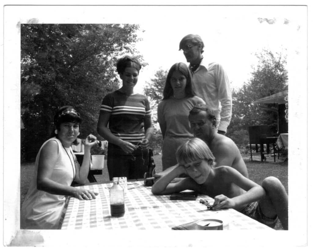 Black-and-white family photograph of Richard (Dick) seated with family members around an outdoor table, a moment from his life before his passing.