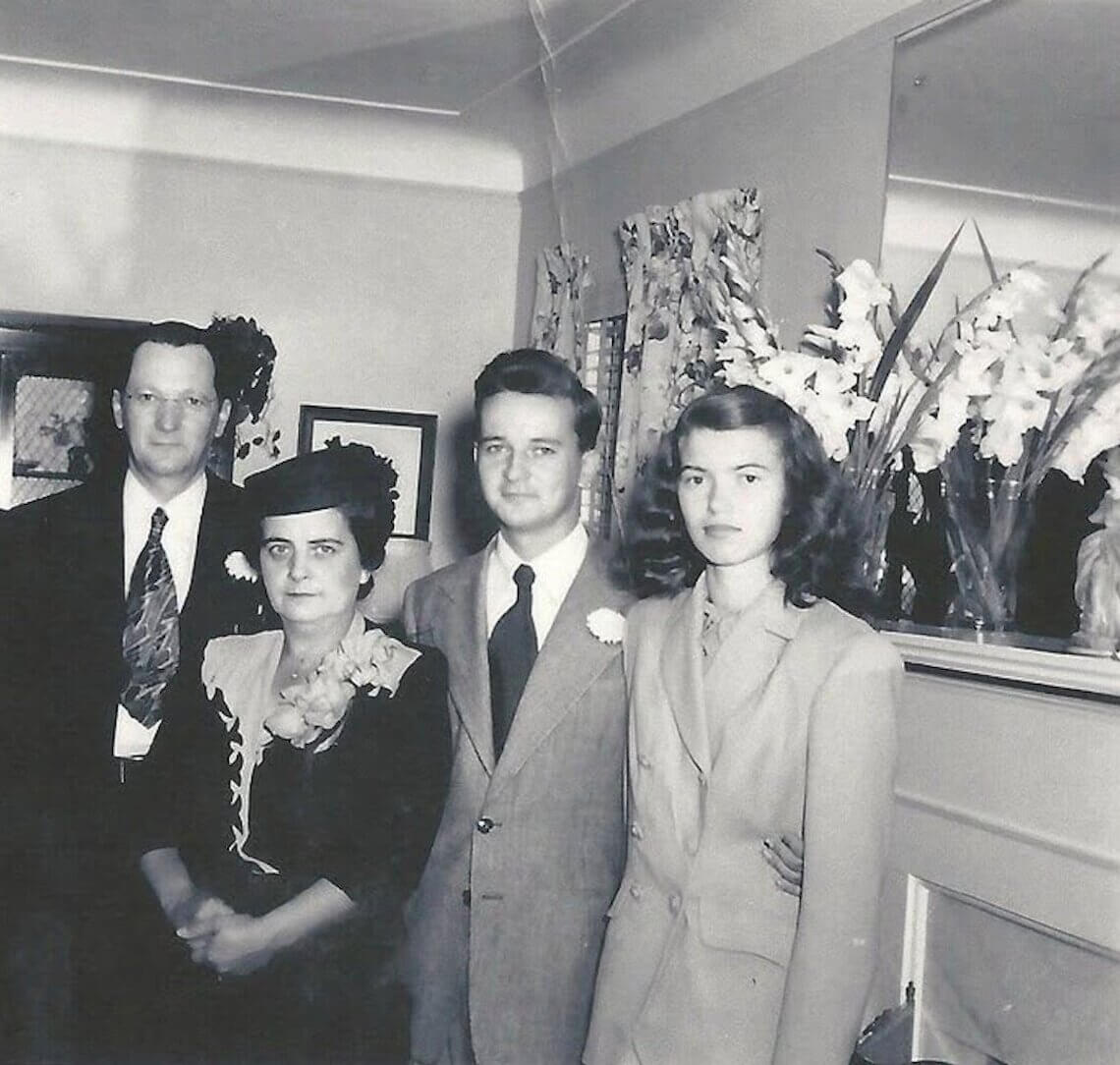 Black-and-white photograph of Richard and his wife, Loraine, standing together at their at-home wedding, surrounded by family members and floral arrangements.